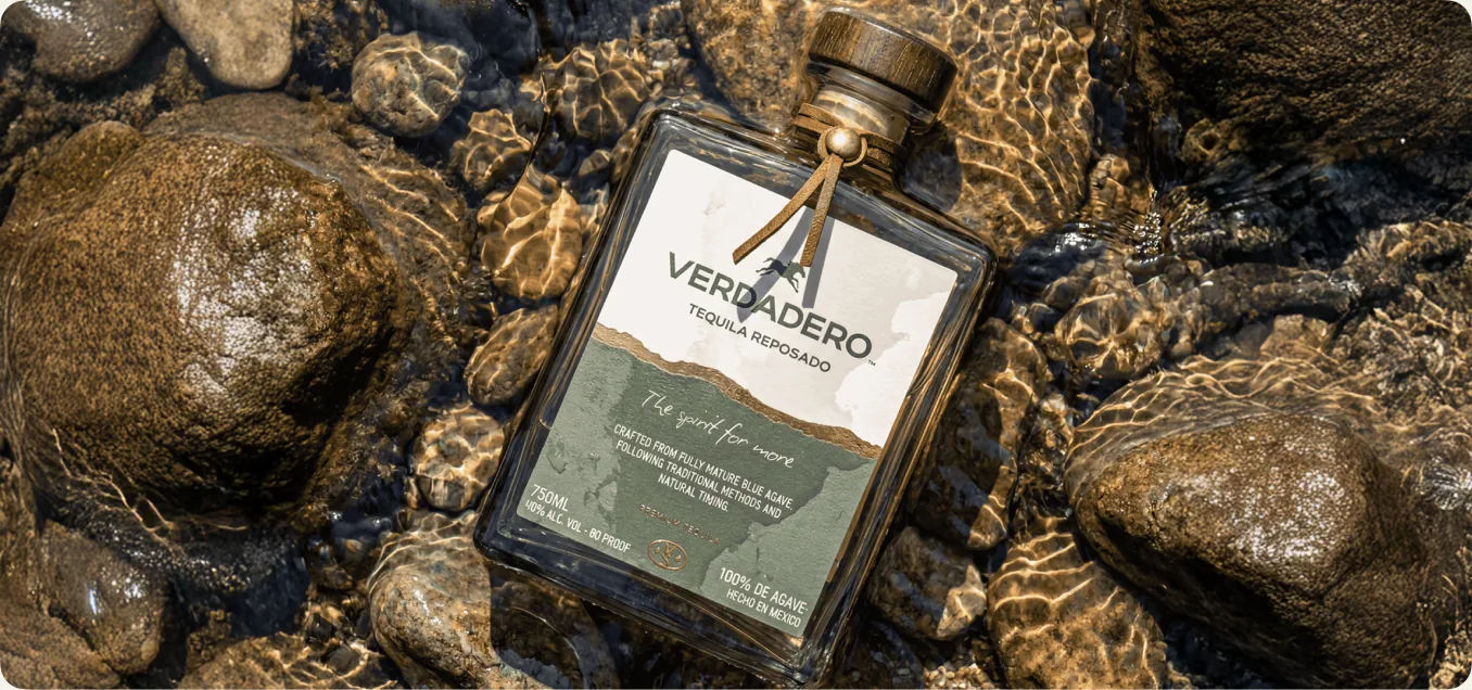 A single Verdadero tequila bottle set on a rocky desert-nature scene with warm afternoon light
