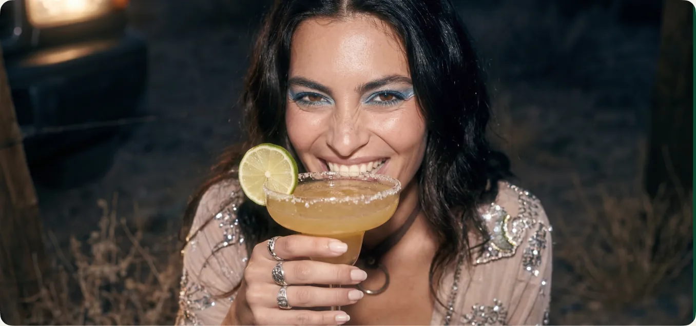 A portrait of a woman holding a Verdadero cocktail in a warm, low-lit interior