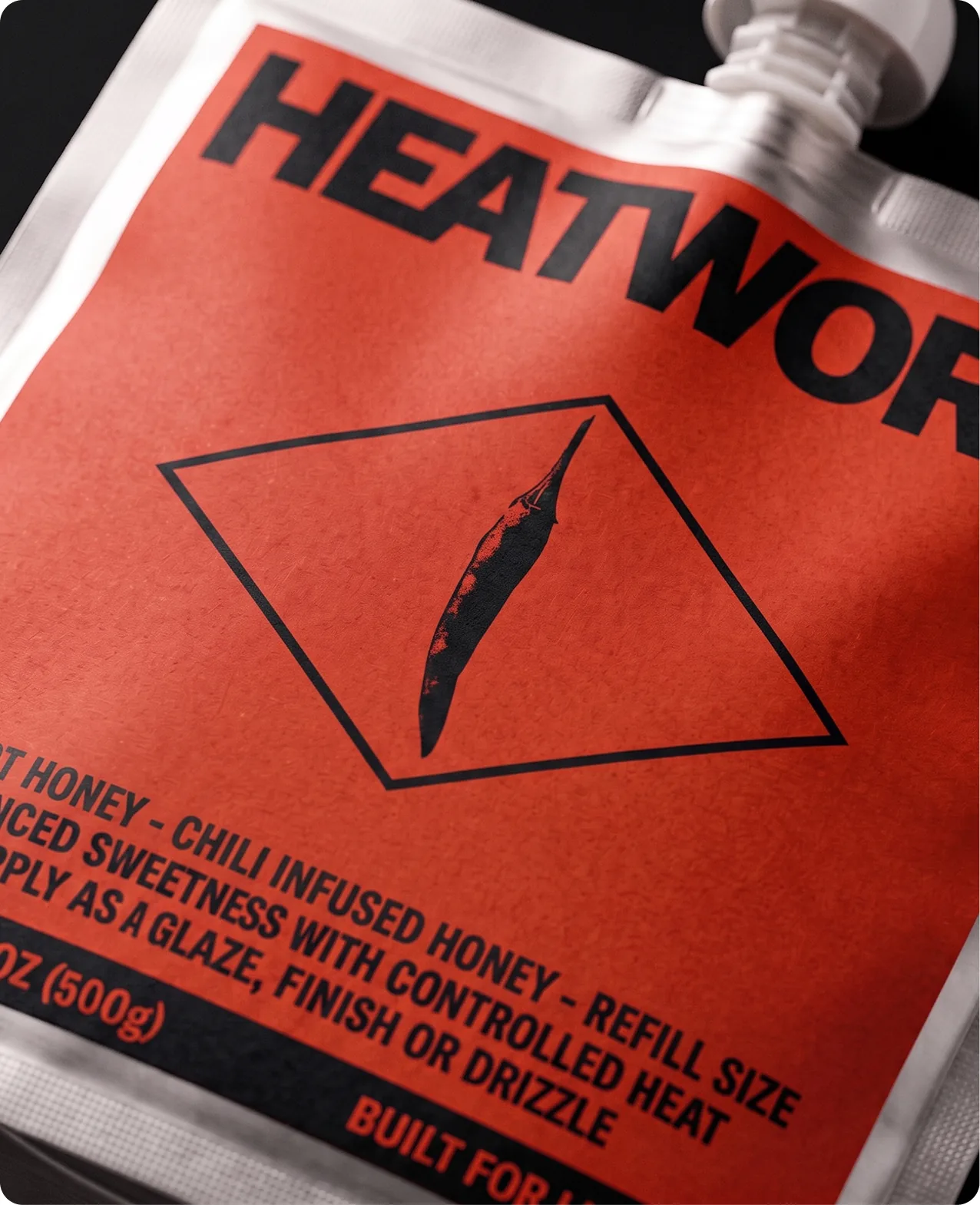 Heatwork: an extreme close-up of the refill pouch, the HEATWORK wordmark running off the edge above the chilli-in-a-diamond mark and the product lines reading hot honey, chili infused honey, refill size