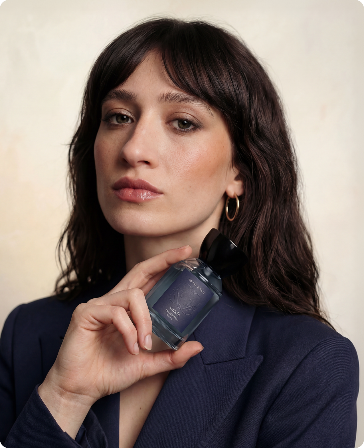 Rouge & Tate — model in a navy blazer holding the Oracle bottle to her jaw, editorial portrait against a cream backdrop