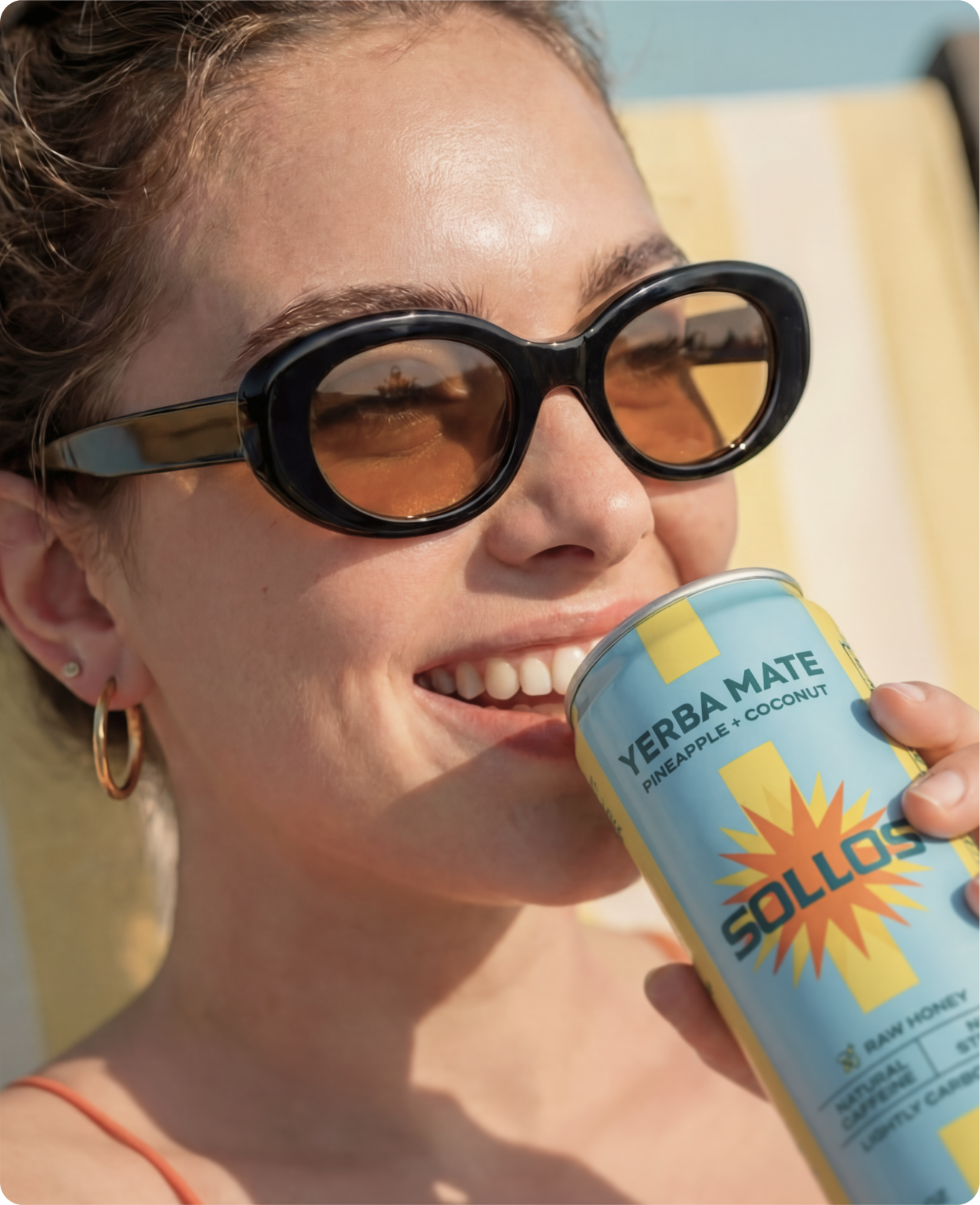 Sollos — a woman in oversized sunglasses smiling while drinking a Sollos yerba mate can in the sun