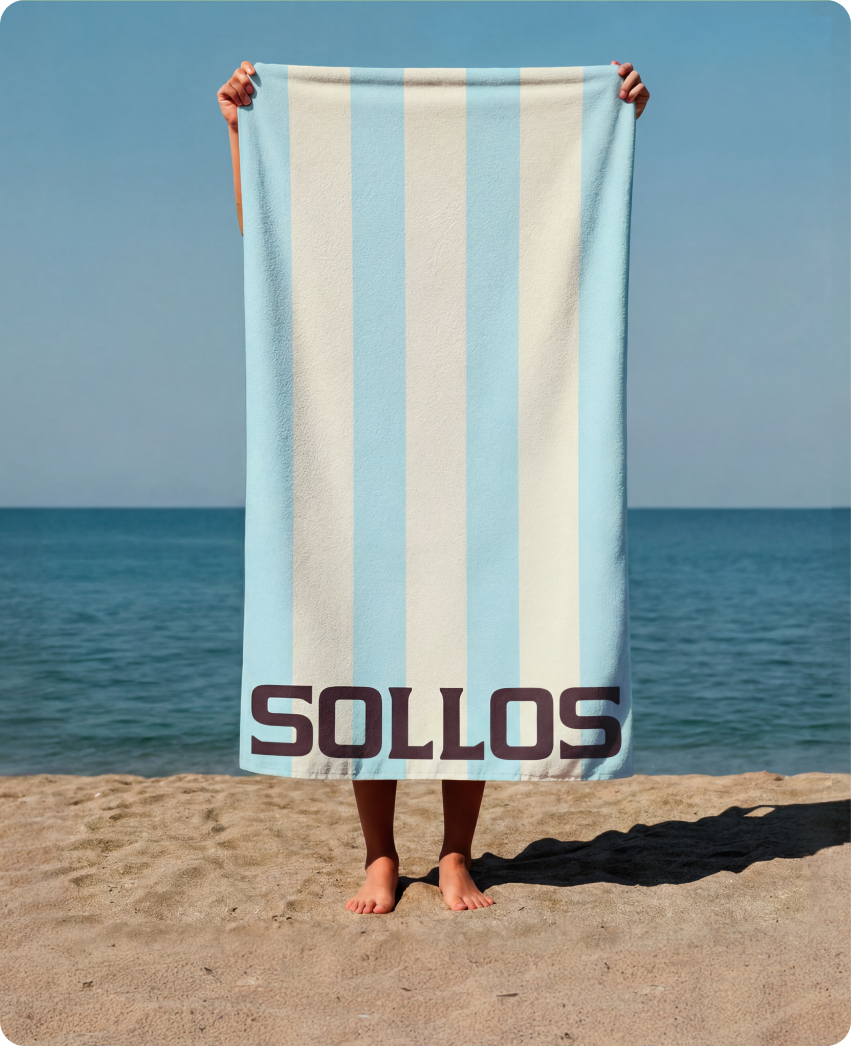 Sollos — a person holding up a sky-blue and cream striped Sollos beach towel on the shoreline