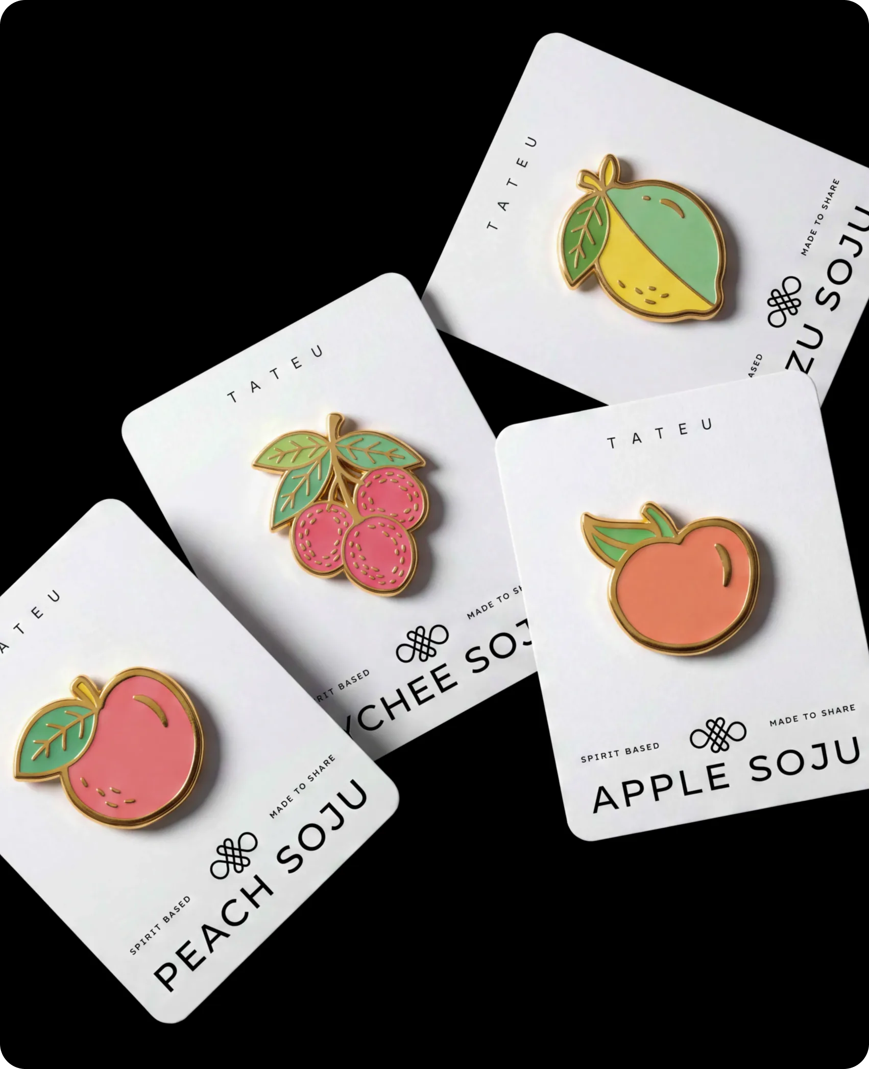 Tateu — enamel flavour pins on individual backing cards against black, a peach, a bunch of lychees and a yuzu each pinned above their flavour name: PEACH SOJU, LYCHEE SOJU, APPLE SOJU and YUZU SOJU