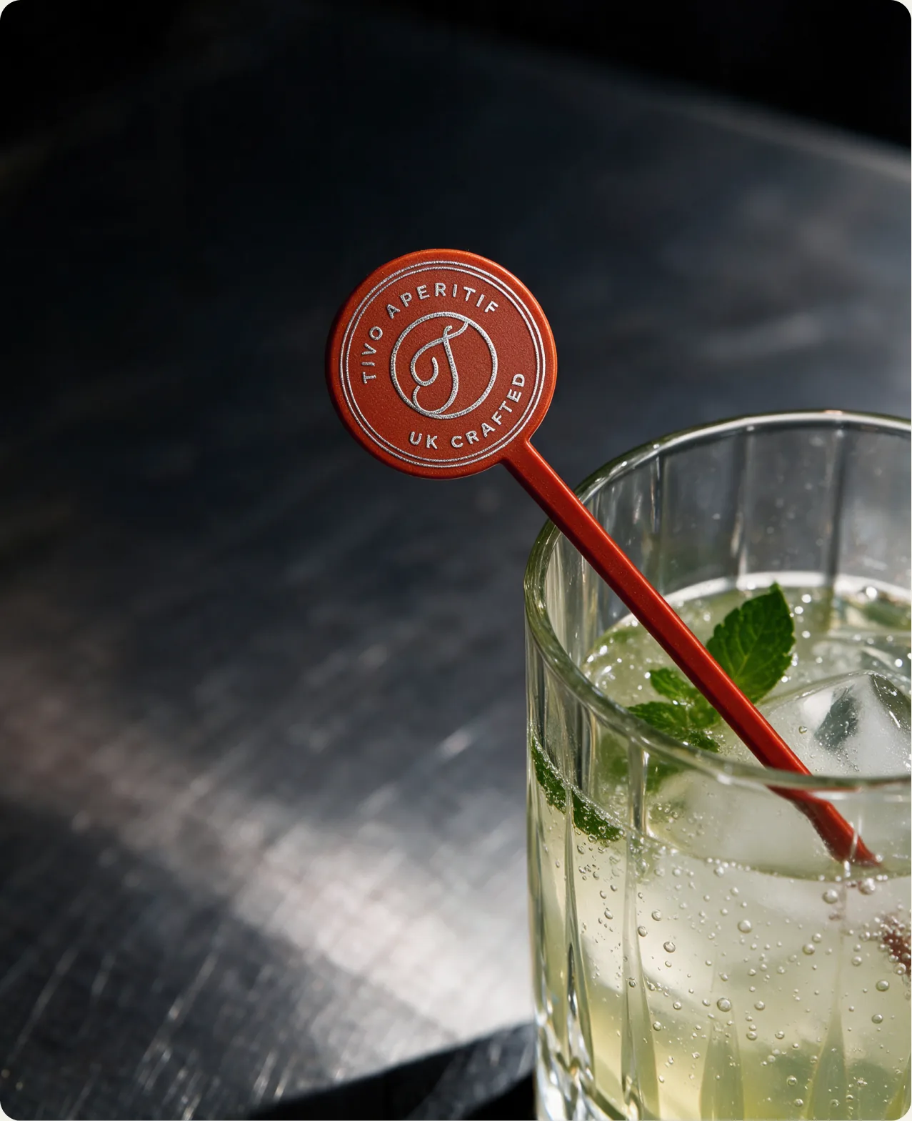 Tivo: a tall iced highball with mint, a red Tivo swizzle stick resting against the rim, its disc reading Tivo aperitif, uk crafted around the cursive T